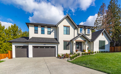 Wide angle shot of front view of luxury two garage big white home with luscious green grass  on a...