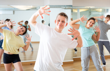 Fototapeta na wymiar Portrait of positive teenage boy exercising in group with friends during dance class