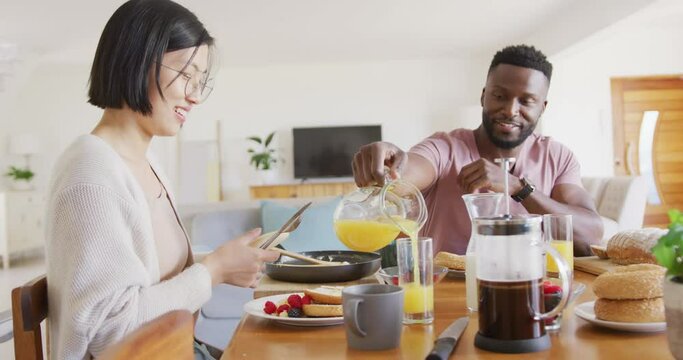 Happy diverse couple sitting at table and having breakfast