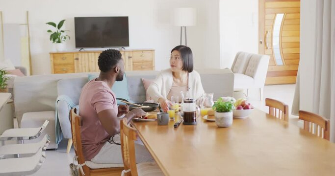 Happy diverse couple sitting at table and having breakfast