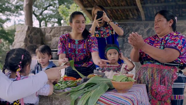 Una familia prepara tamales con hojas de milpa, plato tradicional guatemalteco, mientras la hija mayor graba un video con su celular.