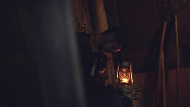 Adult seriously man with beard write old diary wear a vintage leather jacket in retro small fishing house of wood at deep night. Vintage a kerosene lamp fire