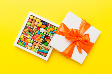 Set of different sweet candy in a paper box with a satin ribbon on a colored background. Holiday concept