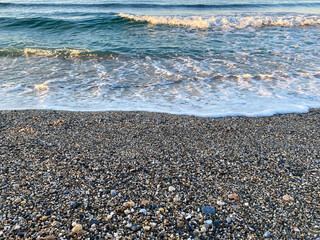 Waves of water in the sea and sand with small natural multi-colored stones on the seashore, small pebbles on the beach. Background, texture