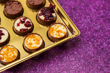 Golden box with delicious chocolate candies on purple table