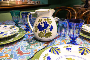 White ceramic plates on a shelf in a store. Designer ceramic plates with a pattern. tableware and eating concept. White jug with roses for table setting with glasses for wine and a bottle for water.