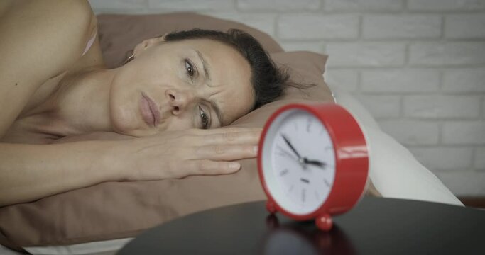 Fatigue woman no sleep. A view of a tired woman unable to sleep at night lay in the bed by the clock.