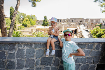 Fototapeta premium Baby girl tourist with brother against panoramic view of the ancient city of Pompeii.