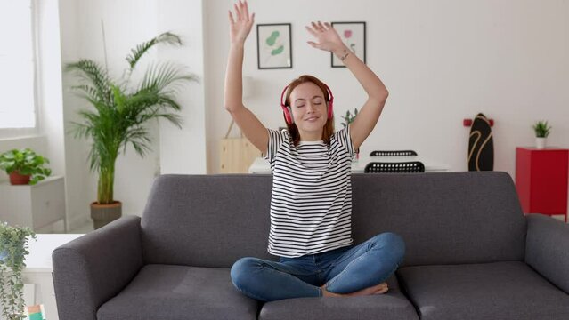 Happy young woman having fun dancing on sofa at home. Domestic lifestyle and happiness concept