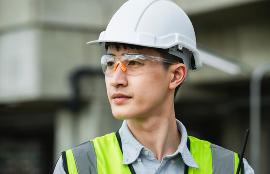 Portrait Of Asian Young Handsome Confident Engineer Wearing Safety Goggles And White Hard Hat In Construction Site Outdoors