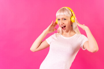 Blonde caucasian girl in studio on pink background, smiling listening to music with headphones