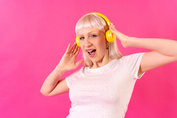 Blonde caucasian girl in studio on pink background, dancing and listening to music with headphones