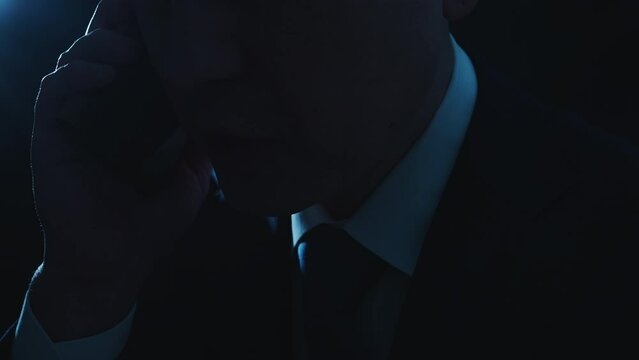 暗い部屋でスマートフォンで電話をかけているスーツを着たビジネスマンの男性