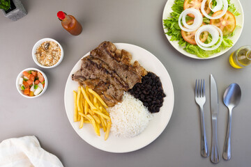 Delicious executive dish of beef steak, rice, beans, french fries and green salad with lettuce, tomato and onion accompanied by farofa and vinaigrette. Typical Brazilian food. Selective focus