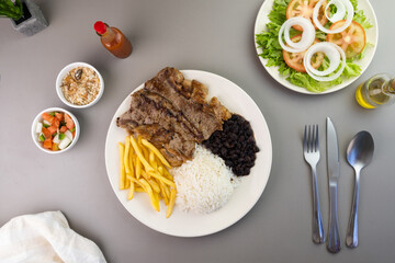 Delicious executive dish of beef steak, rice, beans, french fries and green salad with lettuce, tomato and onion accompanied by farofa and vinaigrette. Typical Brazilian food. Selective focus