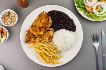 Delicious executive dish of chicken fillet, rice, beans, french fries and green salad with lettuce, tomato and onion accompanied by farofa and vinaigrette. Typical Brazilian food. Selective focus