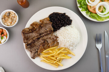 Delicious executive dish of beef steak, rice, beans, french fries and green salad with lettuce, tomato and onion accompanied by farofa and vinaigrette. Typical Brazilian food. Selective focus