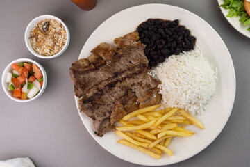 Delicious executive dish of beef steak, rice, beans, french fries and green salad with lettuce, tomato and onion accompanied by farofa and vinaigrette. Typical Brazilian food. Selective focus