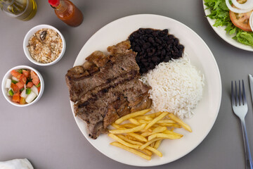 Delicious executive dish of beef steak, rice, beans, french fries and green salad with lettuce, tomato and onion accompanied by farofa and vinaigrette. Typical Brazilian food. Selective focus