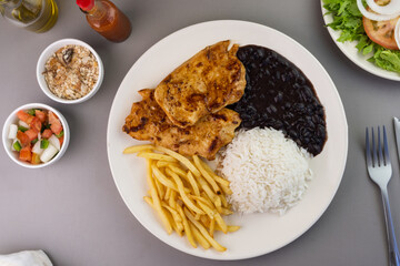 Delicious executive dish of chicken fillet, rice, beans, french fries and green salad with lettuce, tomato and onion accompanied by farofa and vinaigrette. Typical Brazilian food. Selective focus