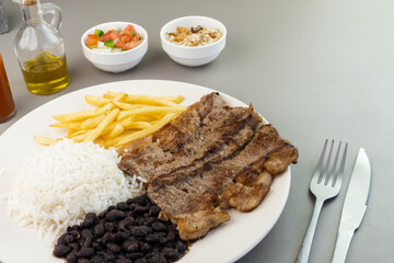Delicious executive dish of beef steak, rice, beans, french fries and green salad with lettuce, tomato and onion accompanied by farofa and vinaigrette. Typical Brazilian food. Selective focus