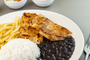 Delicious executive dish of chicken fillet, rice, beans, french fries and green salad with lettuce, tomato and onion accompanied by farofa and vinaigrette. Typical Brazilian food. Selective focus