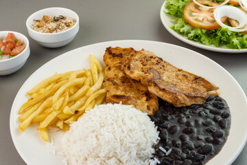 Delicious executive dish of chicken fillet, rice, beans, french fries and green salad with lettuce, tomato and onion accompanied by farofa and vinaigrette. Typical Brazilian food. Selective focus
