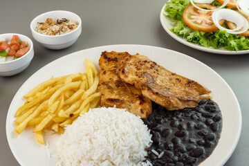 Delicious executive dish of chicken fillet, rice, beans, french fries and green salad with lettuce, tomato and onion accompanied by farofa and vinaigrette. Typical Brazilian food. Selective focus
