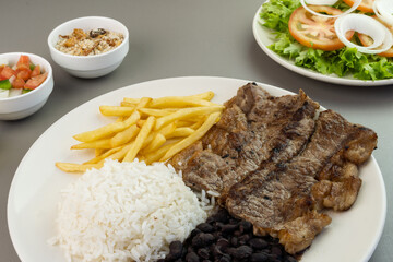 Delicious executive dish of beef steak, rice, beans, french fries and green salad with lettuce, tomato and onion accompanied by farofa and vinaigrette. Typical Brazilian food. Selective focus