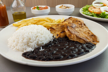 Delicious executive dish of chicken fillet, rice, beans, french fries and green salad with lettuce, tomato and onion accompanied by farofa and vinaigrette. Typical Brazilian food. Selective focus