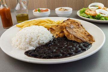 Delicious executive dish of chicken fillet, rice, beans, french fries and green salad with lettuce, tomato and onion accompanied by farofa and vinaigrette. Typical Brazilian food. Selective focus