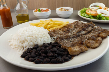 Delicious executive dish of beef steak, rice, beans, french fries and green salad with lettuce, tomato and onion accompanied by farofa and vinaigrette. Typical Brazilian food. Selective focus