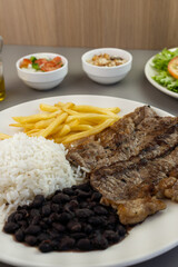 Delicious executive dish of beef steak, rice, beans, french fries and green salad with lettuce, tomato and onion accompanied by farofa and vinaigrette. Typical Brazilian food. Selective focus
