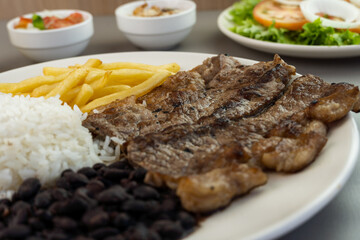 Delicious executive dish of beef steak, rice, beans, french fries and green salad with lettuce, tomato and onion accompanied by farofa and vinaigrette. Typical Brazilian food. Selective focus