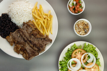 Delicious executive dish of beef steak, rice, beans, french fries and green salad with lettuce, tomato and onion accompanied by farofa and vinaigrette. Typical Brazilian food. Selective focus