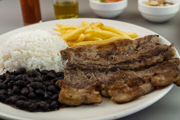 Delicious executive dish of beef steak, rice, beans, french fries and green salad with lettuce, tomato and onion accompanied by farofa and vinaigrette. Typical Brazilian food. Selective focus