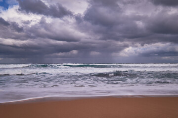 Storm clouds over rough ocean seas with waves breaking onto a sandy beach, beautiful coastal location in Victoria, Australia.