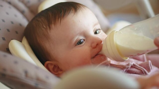 6 month old baby drinks milk from a bottle. happy family dream weaning concept. grimy baby girl eats milk from a bottle in a indoors high chair