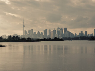 Fototapeta na wymiar Autumn day view across inner bays of Lake Ontario in Tommy Thompson Park with foggy Downtown Toronto skyline under grey cloudy skies in background with water surface reflecting the buildings outlines