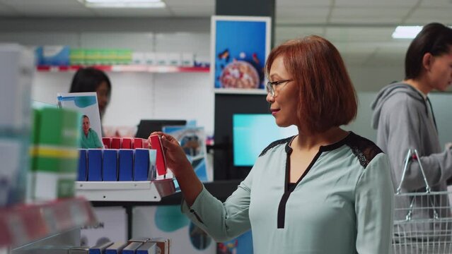 Female buyer looking at pharmaceutical products to find medicine, analyzing packages of medicaments on shelves. Woman searching for pills and supplements, pharmacy shop. Handheld shot.