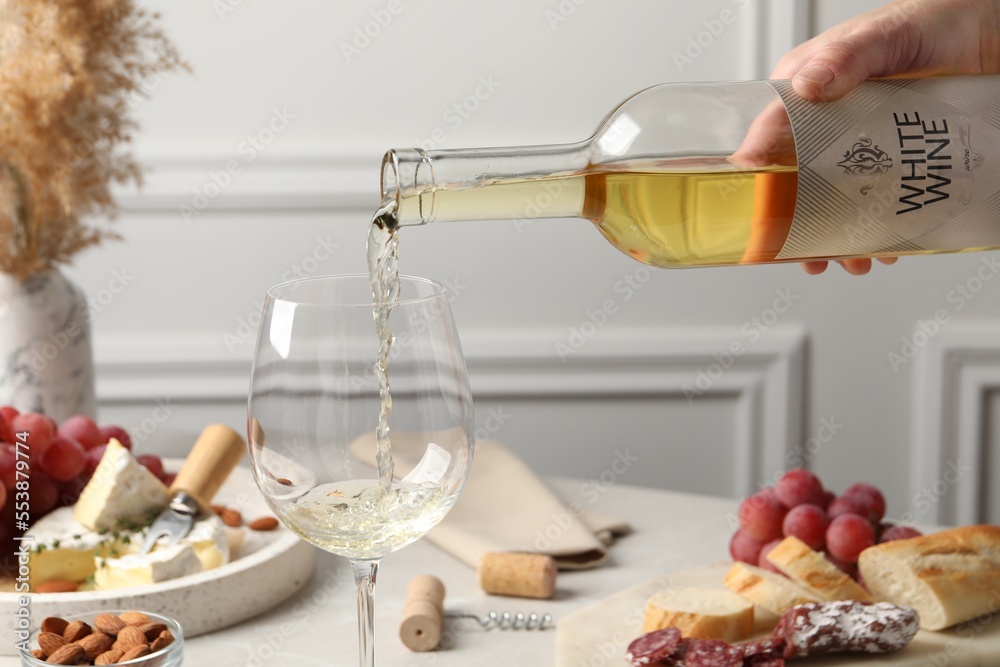 Poster Woman pouring white wine from bottle into glass at table with snacks, closeup