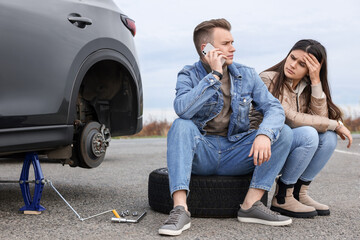 Young man calling to car service on roadside. Tire puncture