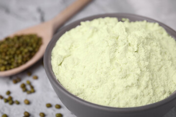 Mung bean flour in bowl and seeds on white textured table, closeup