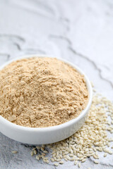 Sesame flour in ceramic bowl on white textured table
