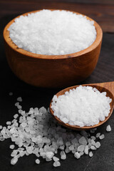 Fototapeta na wymiar Spoon and bowl of natural sea salt on wooden table, closeup