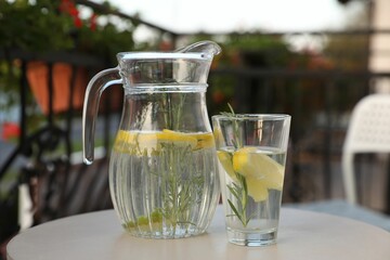 Jug and glass with refreshing lemon water on light table outdoors