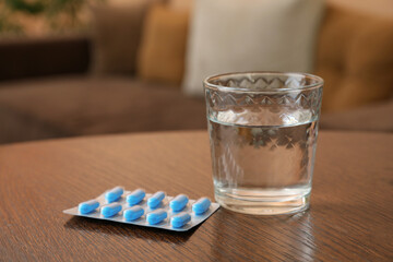 Glass of water and pills on wooden table indoors, space for text. Potency problem concept