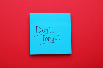 Paper note with phrase Don't Forget on red background, top view