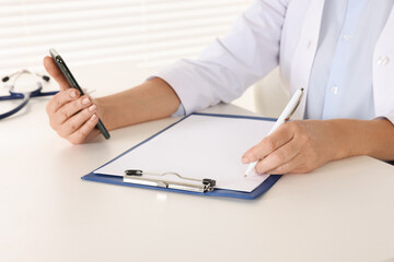 Doctor with smartphone and clipboard at desk indoors, closeup. Online medicine concept