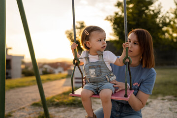 mother and daughter little toddler girl child on swing in park